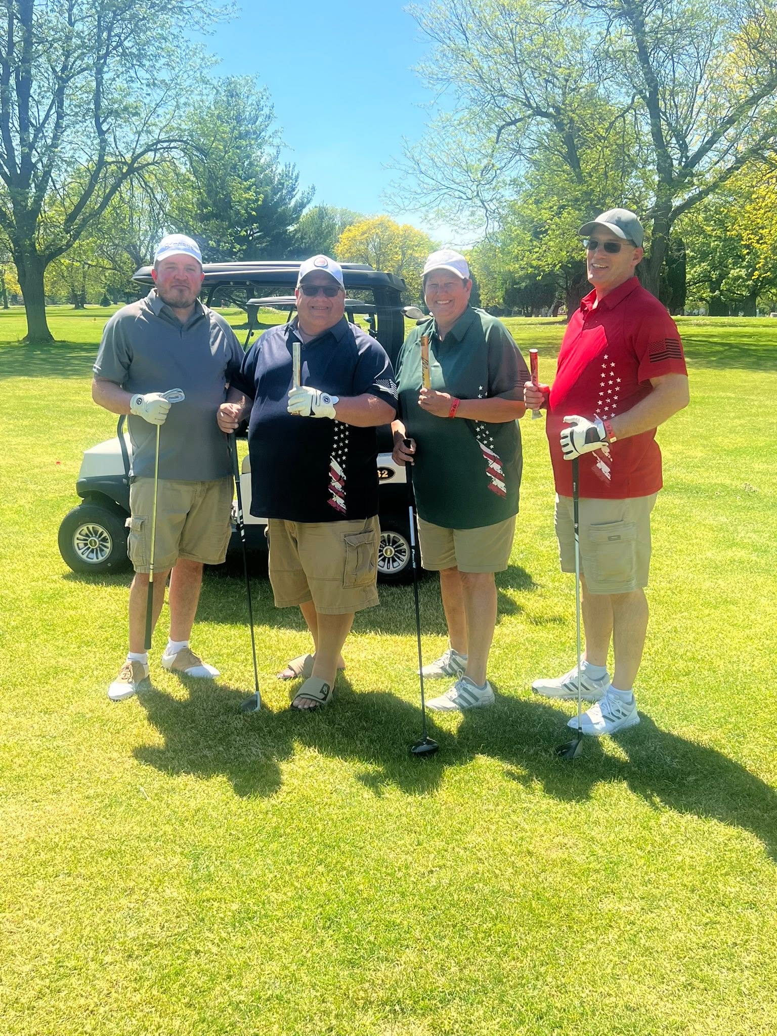 Four golfers holding clubs beside a golf cart on the tree-lined course at Columbus Country Club
