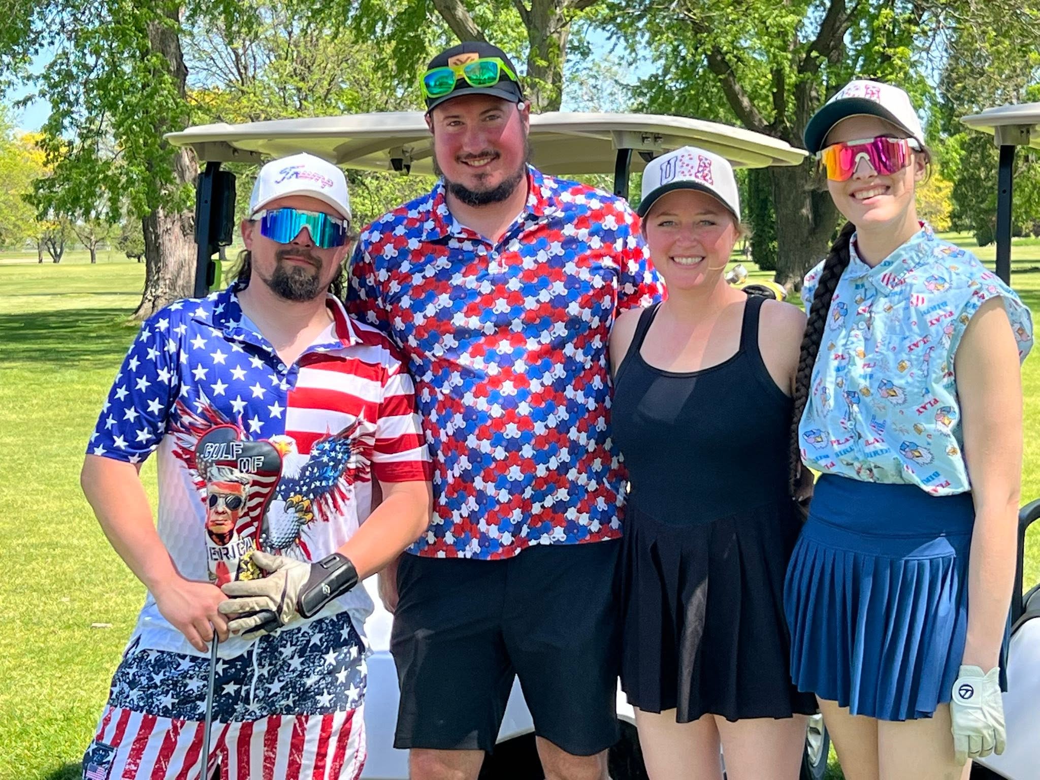 Four smiling outing participants standing together beside golf carts at Columbus Country Club